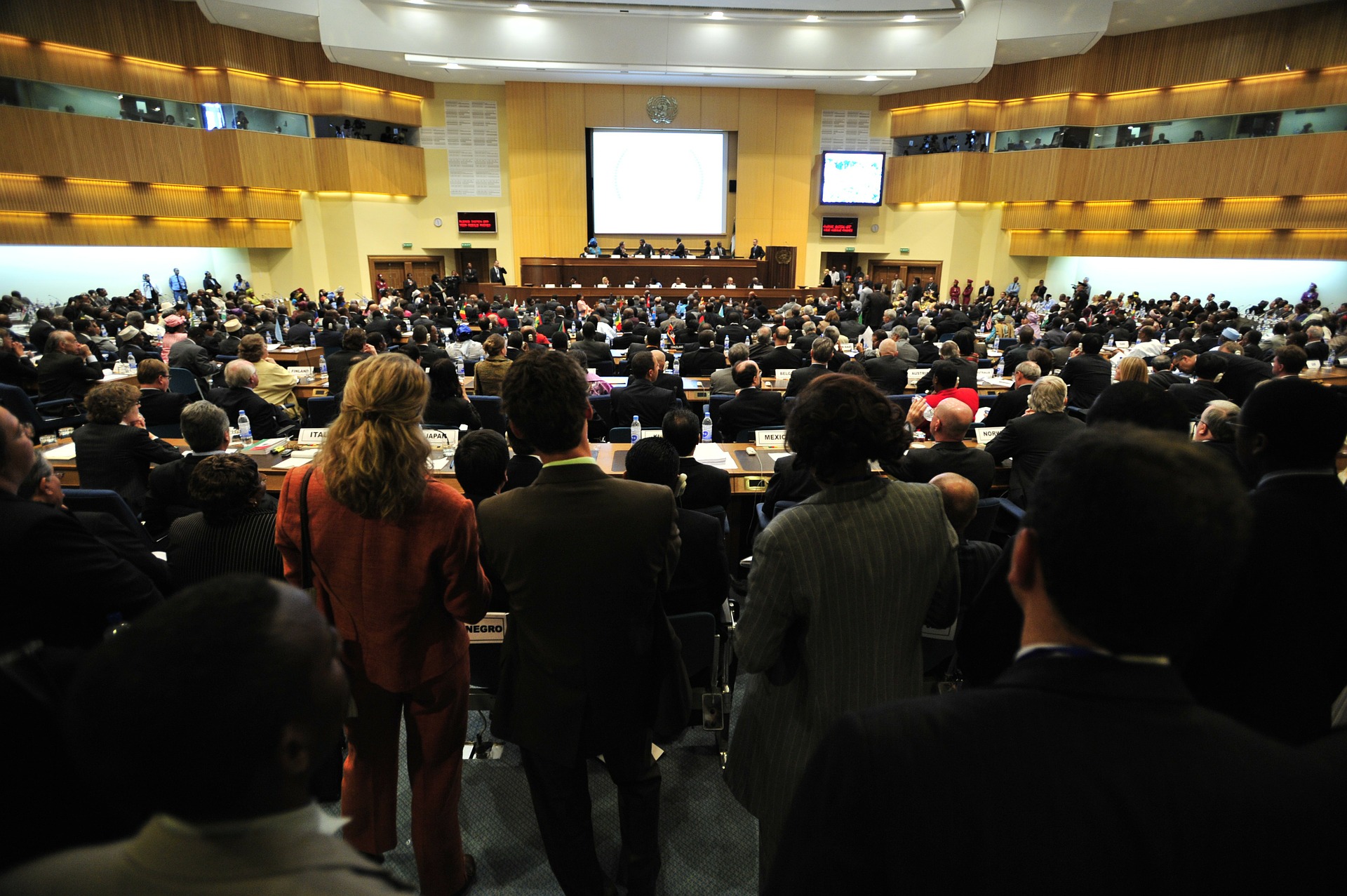 A crowded government conference takes place in an assembly hall equipped with ASI Architectural acoustic wooden panels and ceiling tiles.