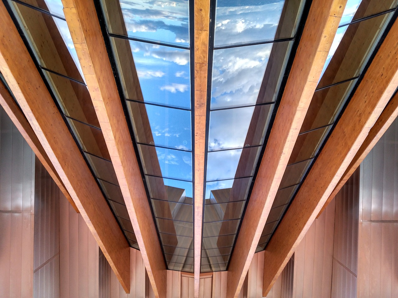 A sky light made of ASI Architectural acoustic wooden beams and glass offers a view of a cloudy sky
